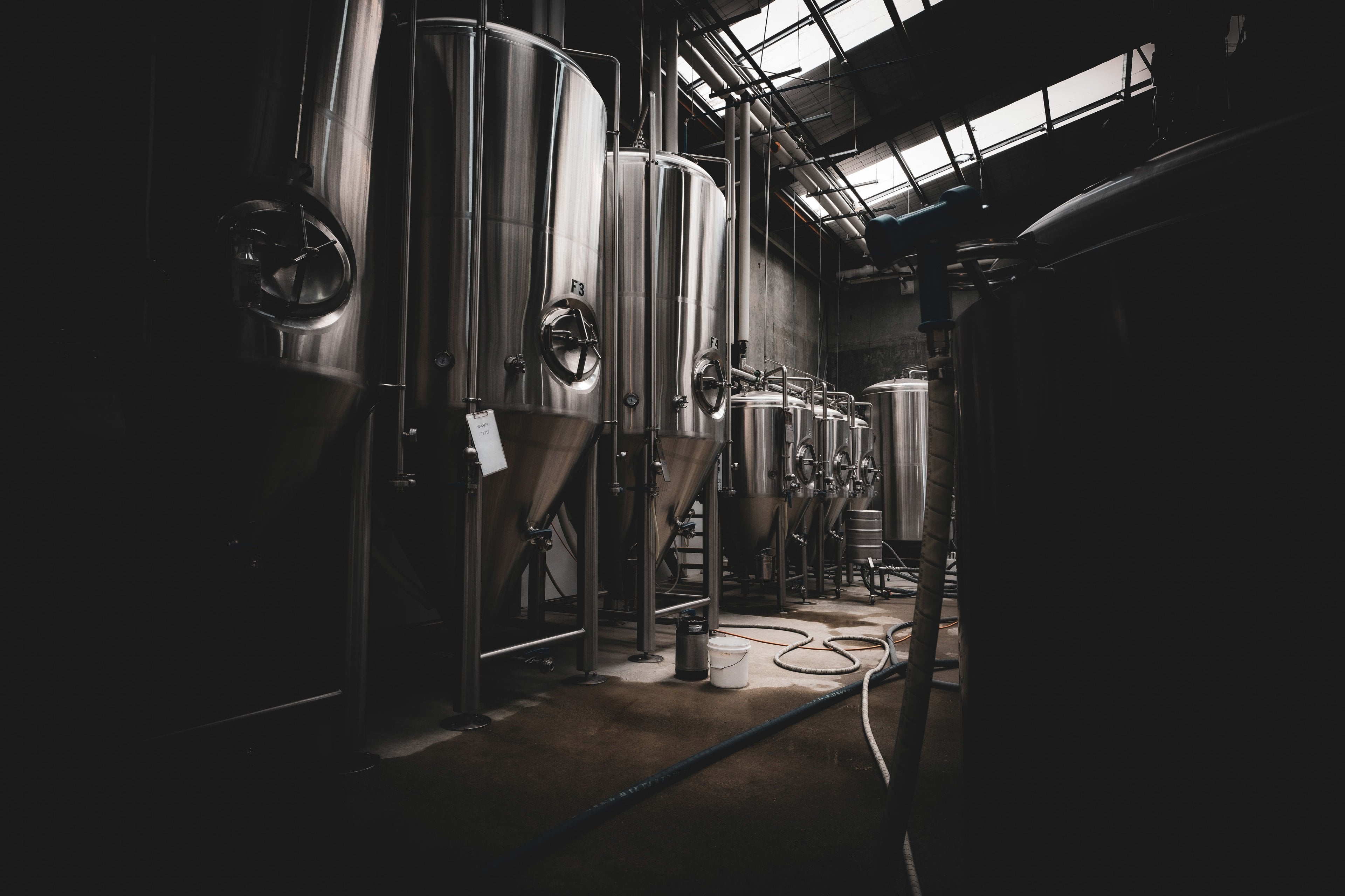 Rangée de cuves de fermentation en acier inoxydable poli dans la cave faiblement éclairée d’une brasserie